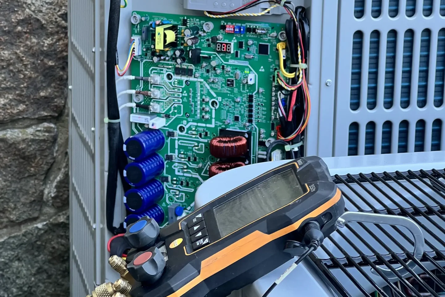 Technician testing electrical controls inside an open outdoor AC condenser