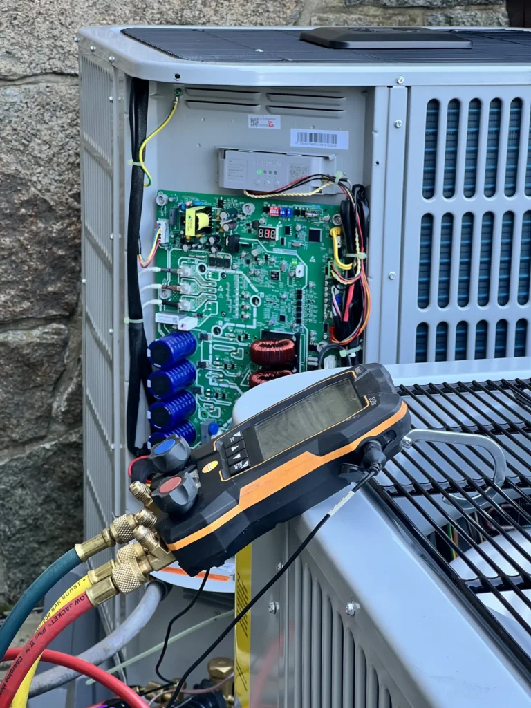 Technician testing electrical controls inside an open outdoor AC condenser
