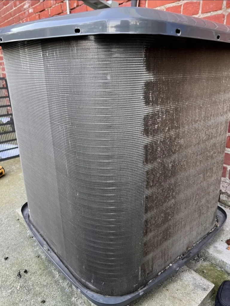 Outdoor AC condenser coil visibly clogged with dirt before cleaning