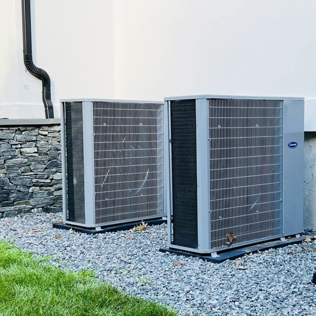 Two Carrier outdoor AC condensers installed beside a home on clean equipment pads