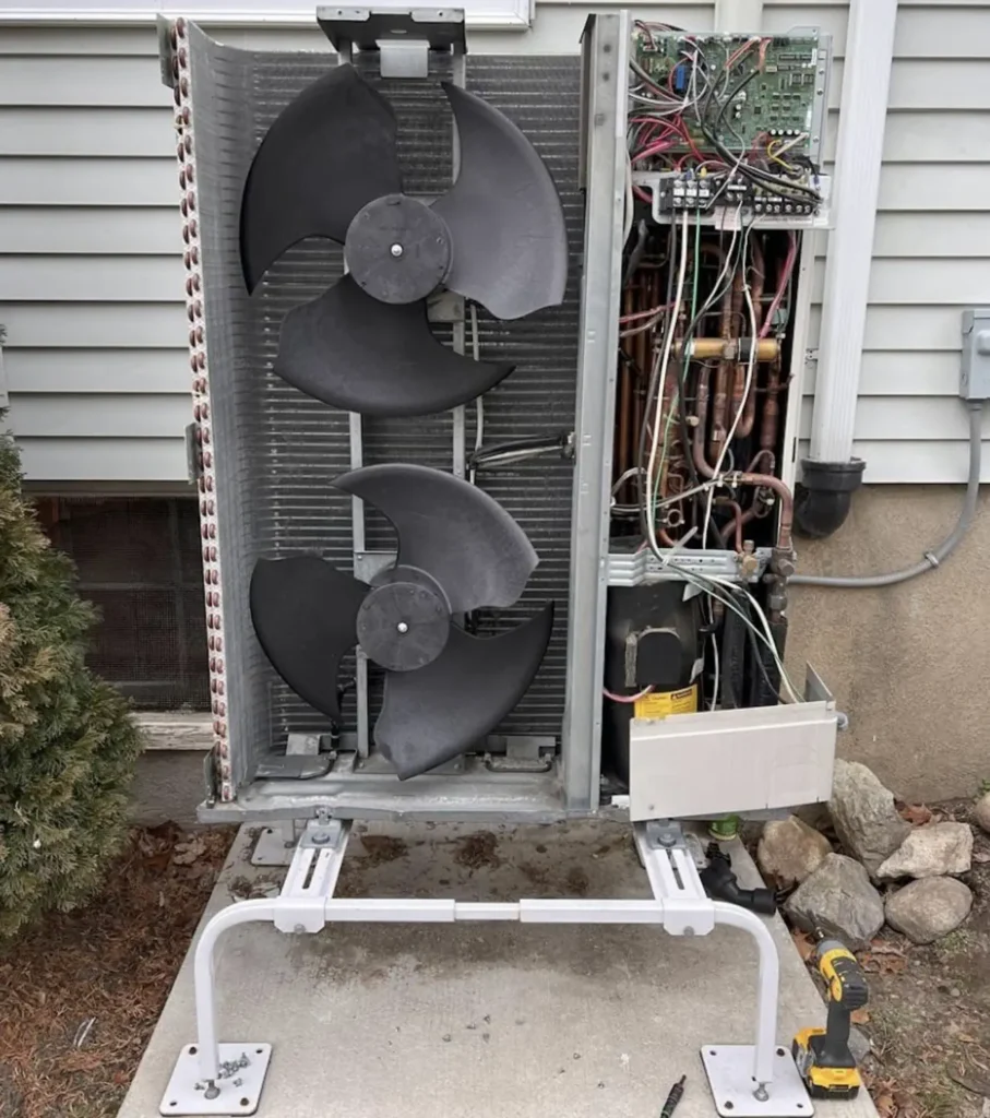 Open dual-fan heat-pump outdoor unit showing coils, fans, and electrical controls