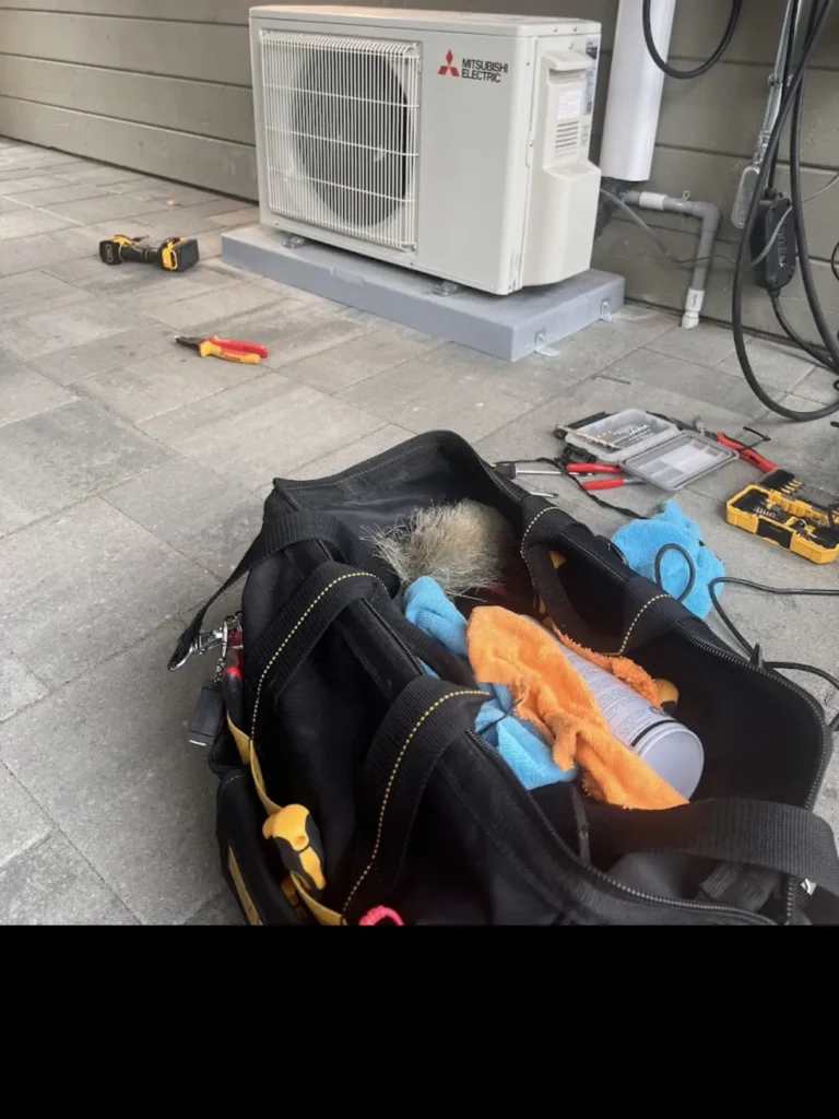 HVAC technician servicing a ductless outdoor heat pump with tools nearby