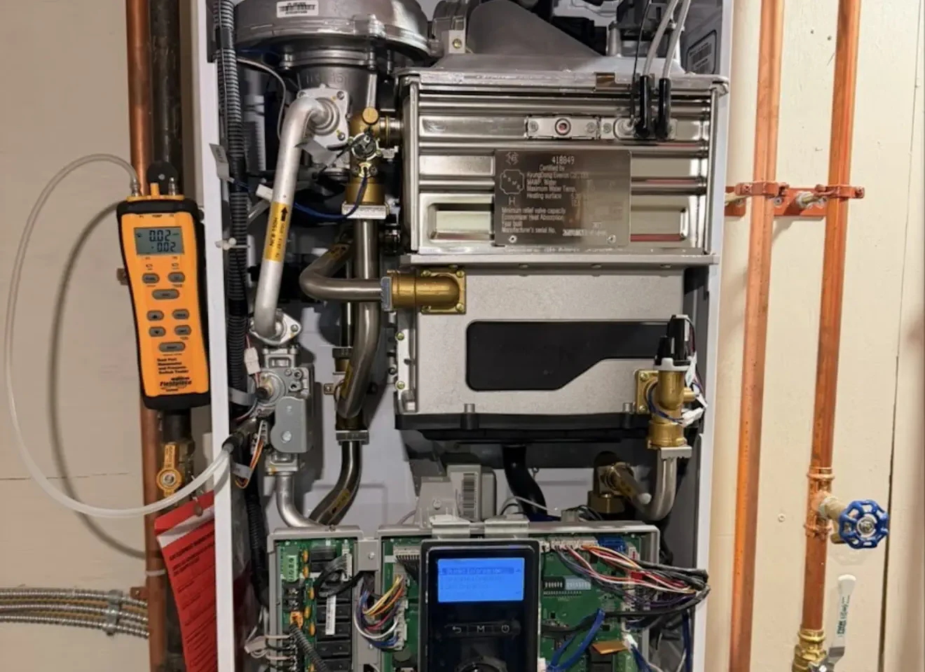 Open Navien combi boiler being tested with a digital multimeter