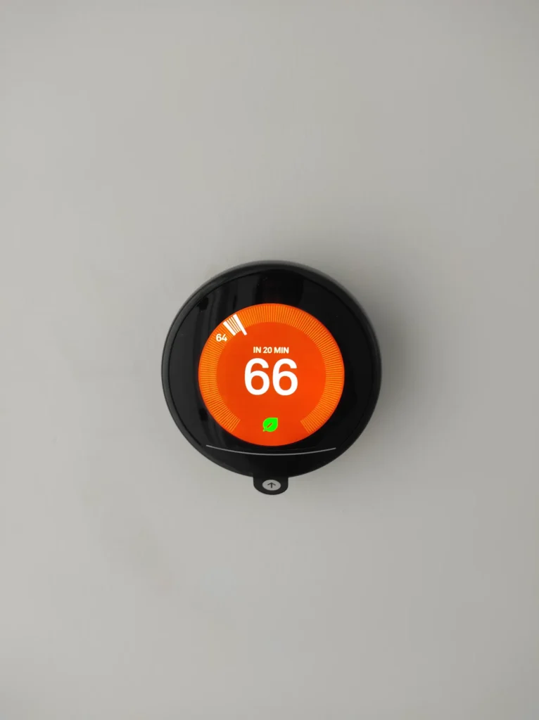 Round Nest smart thermostat displaying 66 degrees on a finished wall