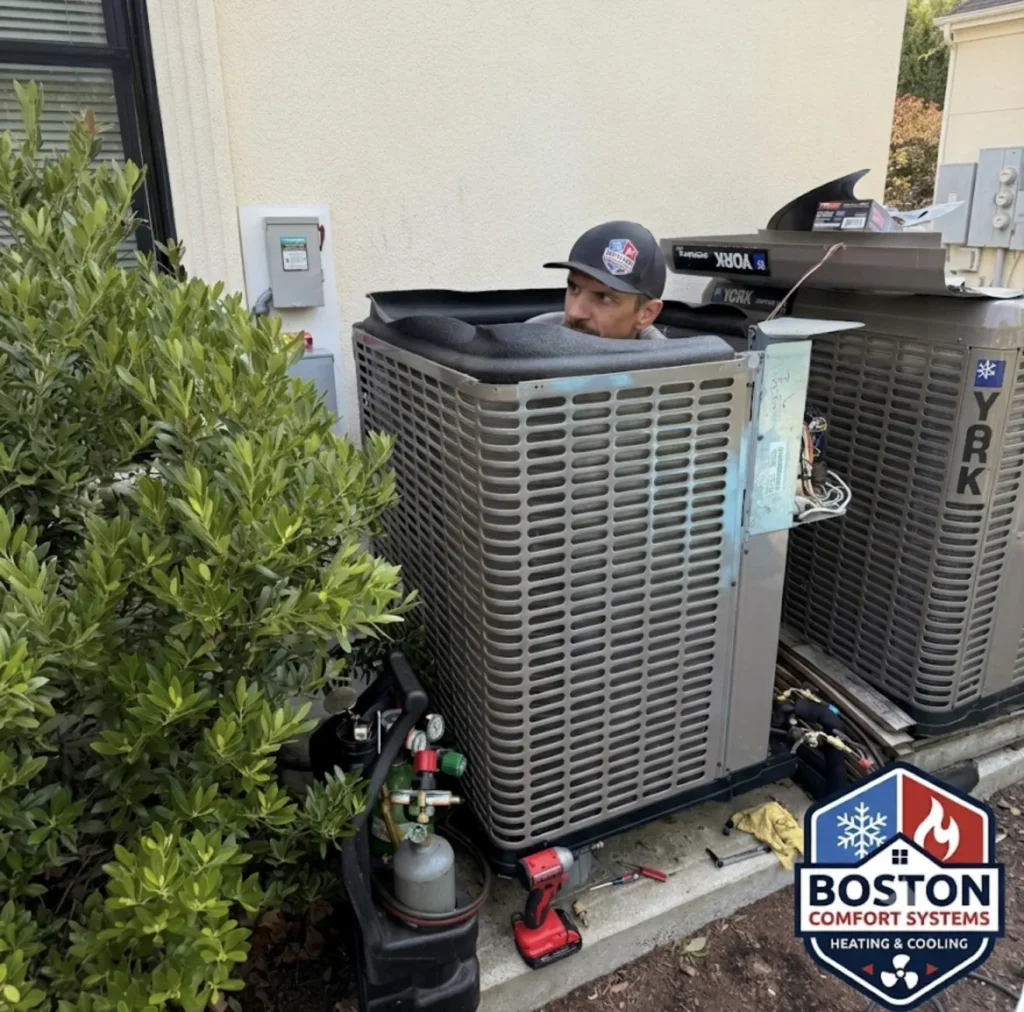 Boston Comfort Systems technician repairing electrical components inside an outdoor condenser